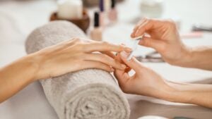 Close up shot of a woman in a nail salon receiving manicure by beautician with metal nail file. Woman getting nail manicure at spa centre. Beautician file nails to a customer in luxury salon.